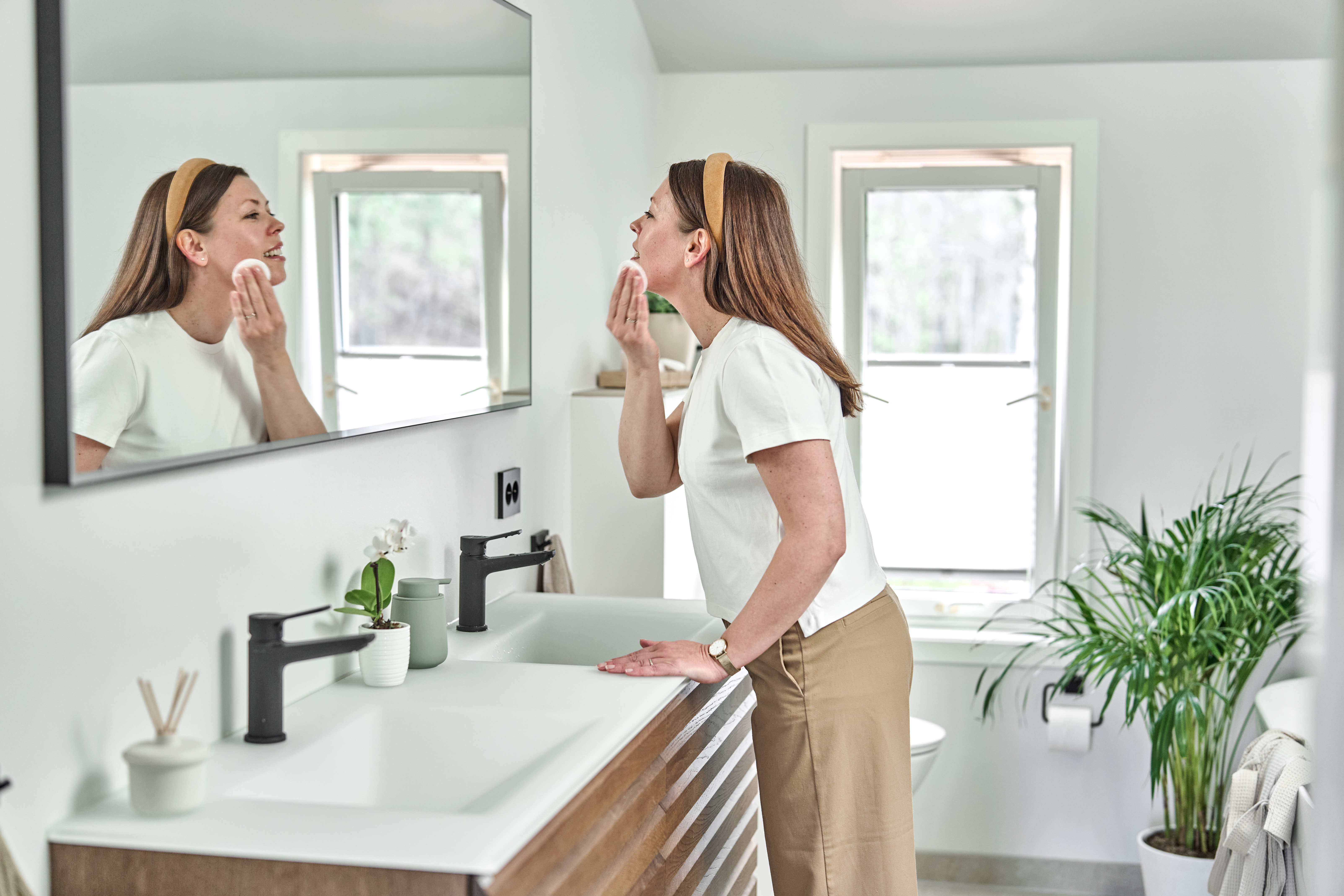 Kvinne står foran speilet på badet og fjerner sminke
